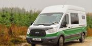 A green and white Karen & Co. campervan parked on a forest road