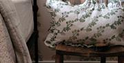 A ruffled cushion with a green print sits on a chair next to a bed.