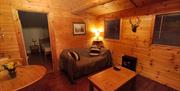 Pine-clad warmly lit living area with 2 seater sofa & fur cushions, TV, dining area, warm tartan curtains and dimmable antler chandelier