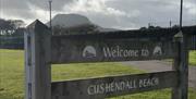 a wooden sign reads 'Welcome to Cushendall Beach', with the Lurig Mountain visible in the background