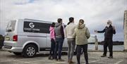 tour guide, Flip, talks to a group of tourists standing beside a van branded with the 'Giant Tours' logo