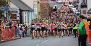 A large group of runners make their way up through the village along the road