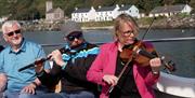 a group play musical instruments (a flute and a violin) while on a boat in Rathlin Island's harbour