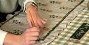 A woman carefully painting a ruffled cushion cover.