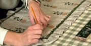 a person uses a paint brush to paint a green border around a ruffled pillow case resting on a green gingham tablecloth