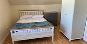 Double bedroom with a white bed, wardrobe and chest of drawers beneath a sloping ceiling.