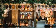 a bartender reaches for a hanging glass at a bar which is decorated with a festive garland