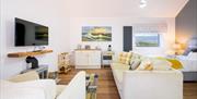 Bright open-plan living and bedroom area in Apple Studio featuring a cream sofa with yellow plaid pillows, wall-mounted TV over an electric stove, and