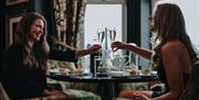 two women clink their prosecco glasses together over a table at Elephant Rock Hotel