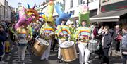 Carnival parade makes its way down the street with performers dressed in bright yellow costumes wearing tall coloured hats