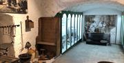 inside view of exhibits in museum looking down a passageway with some items attached to wall, some on floor, and a glass fronted display case on left.