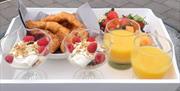 Fresh continental breakfast tray with croissants, berry yogurt parfait bowls, orange juice, and fresh strawberries served outdoors.