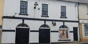 outside view of exterior of Museum building - white historic building with black panels and large arched window and overhanging sign over a black barn