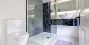 Bright, contemporary en-suite bathroom featuring a modern white toilet, a frameless glass walk-in shower with dark marble-effect wall panels, and a sl