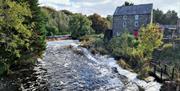 Image showing the River Bush flowing past a brick building with a red door and water wheel at the side