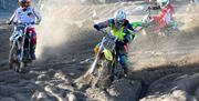 Three motorcycle riders kicking up sand as they compete on the beach