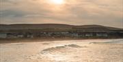 Soft sunlight reflecting off gentle waves with a  Castlerock town and rolling hills in the background under a cloudy sky