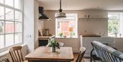 A modern home interior, a table with three chairs sits at the centre of the frame and a small potted flower atop it.