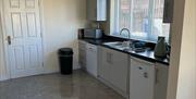 Modern kitchen with white units, black worktops and a large window providing natural light.