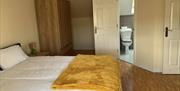 Double bedroom with a wooden wardrobe, bedside table and ensuite bathroom visible through an open door.