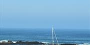 Blue sky and sea in the background, white sailing boat in the foreground with wooden fence atop stone wall left to right at the front