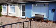 Picture depicting the external view of No.$ self-catering. A blue semi-detached house with white windows and door fronted by a gravel yard and blue ga