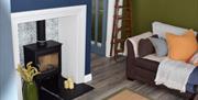 Living room with black wood burning stove situated within a blue chimney breast and tiled alcove, brown sofas with yellow, blue. green and orange acce