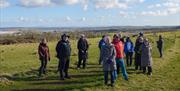 Bob Picken guiding a group in outdoor clothing listening to stories of Downhill House