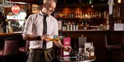 Bartender and mixologist, Ashely, pours whiskey in to a glass in front of a bar.