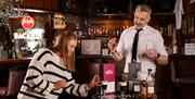 a woman sprays the top of an Irish Coffee with an atomiser while a bartender watches on