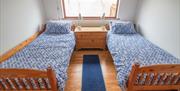 Twin single beds with blue patterned bedding in a bright bedroom with wooden floor and window.