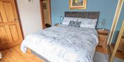 Double bed with grey bedding in a bright bedroom with wooden floor and blue accent wall.