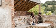 a couple enjoy drinks outside under a wooden shelter