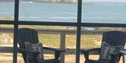 View from inside the living room of the cottage, over the deck seating area, sea and with Sheep Island in the background.