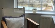 Director's chair with nautical cushion, window behind looking out towards the beach, sea and Sheep Island.