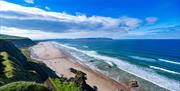 Clifftop view of a Downhill Beach with waves breaking along the shore under a bright blue sky