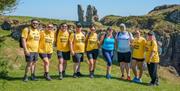 A group of participants in yellow Giant Steps t-shirts standing together on a grassy cliffside with coastal rock formations in the background, smiling