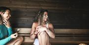 two ladies relax in sauna whilst appyling a face mask
