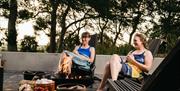 Two ladies relax by the fire pit in their bathing costumes