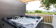 Outdoor hot tub with water jets under a covered wooden deck looking out toward mountain views.