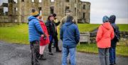 Bob Picken guiding a group in outdoor clothing while looking at the ruins on the Downhill Demesne