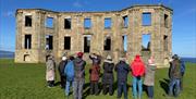 Bob Picken guiding a group in outdoor clothing  while looking at the ruins on the Downhill Demesne