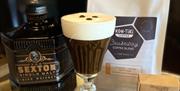 a bottle of Sexton Single Malt whiskey, an Irish Coffee with 3 coffee beans floating on the cream head, a bag of Kon-Tiki Causeway Coffee