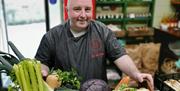 a man stands with a box filled with fresh vegetables including carrots, parsnips, celery, onions and cabbage