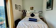 Bedroom with double bed, pictures on the walls. Floor to ceiling window overlooking garden.