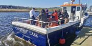 people on a boat docked at a harbour. signage on the boat reads 'Causeway Lass Coleraine'