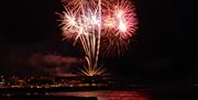 Fireworks burst to life above the sea and rocks, with the college in the background