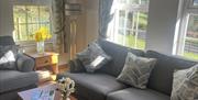Sunlit living room with grey sofas, patterned cushions, and large windows.