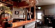 The bar at the Causeway Hotel, a classic looking counter with many wine glasses hanging up above it.