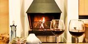 two glasses of red wine sit on a table infront of a lit fire